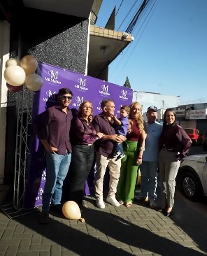 Família e equipe da Mil Malhas na reinauguração da loja no Setor Campinas, em frente ao painel com o logotipo da marca